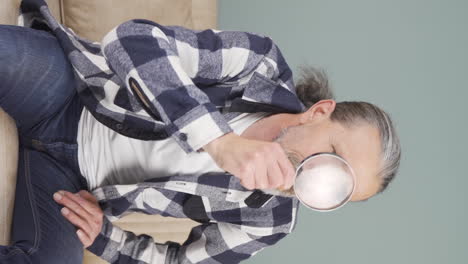 Vertical-video-of-Old-man-looking-at-camera-with-magnifying-glass.